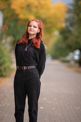 Portrait of a young beautiful red-haired girl in black jeans and a black sweater in an autumn park.