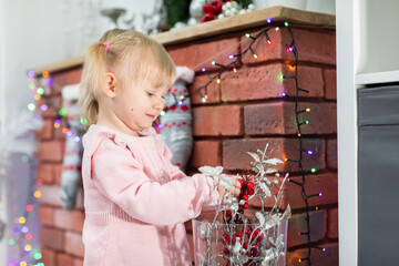 Little girl plays with Christmas decorations set up by the fireplace