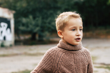 Street portrait of cute blond boy in sweater close-up selective focus