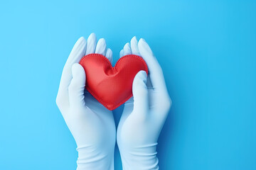 Hands in medical gloves holding a red heart shape model against blue background. Cardiology, organ donation or healthy heart concept.