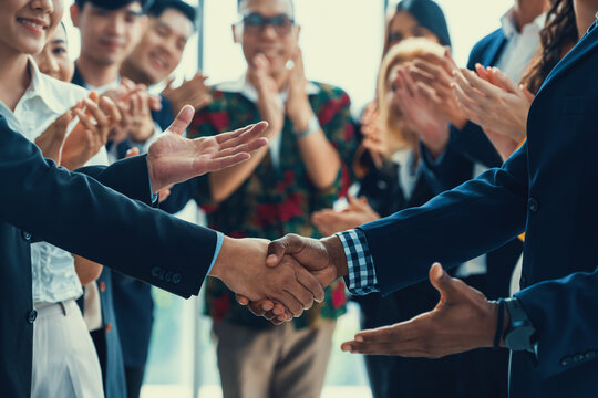 Cropped image of businessmen shaking hand and making a contract in the sign of agreement, cooperation rounded with smiling employees clapping hands and applause behind. Front view. Intellectual.