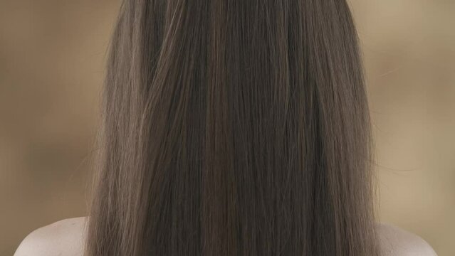 A close-up shot of a middle-aged woman against a blotchy background. She stands with her back to the camera showing off her beautiful dark, long hair. They are straight, shiny and healthy. HDR BT2020