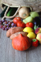 Round straw bag with seasonal fruit and vegetable on wooden background. Late summer or early autumn. Selective focus.