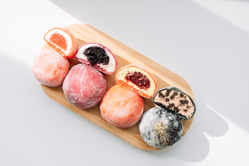 Whole and cut colored mochi on a wooden board on a white background.