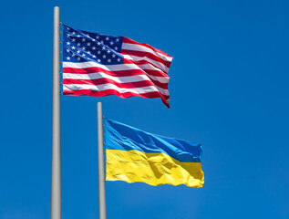 flags of United States and Ukraine waving in the wind against blue sky