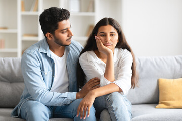 Loving indian man comforting upset wife, sitting on sofa