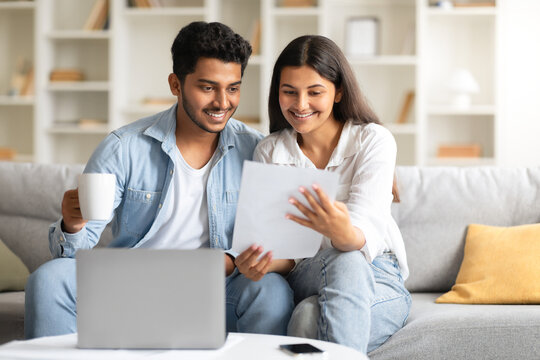 Happy indian couple attentively checking documents and using laptop