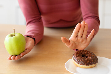 Closeup of lady choosing green apple over donut in kitchen