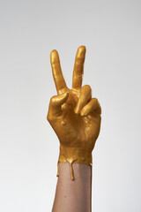 The hand is in gold acrylic paint, the paint covers the hand like a latex glove on light background.