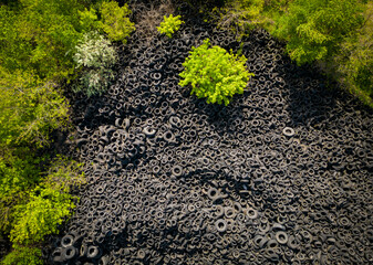 Aerial view of the stark contrast between a massive landfill of used car tires and the surrounding...