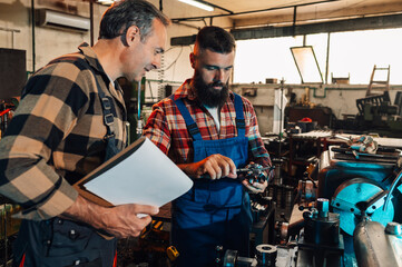 Two metal work artisans checking measures of a metal cylinder, factory.