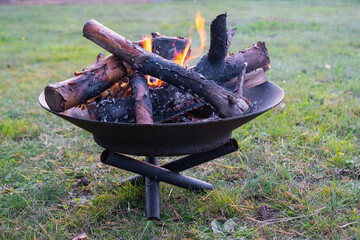 Metal fire bowl with burning wood in the yard. Safe decorative fire pit