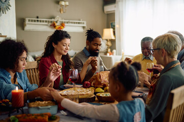 Grateful multigeneration family holding hands while praying at dining table on Thanksgiving.
