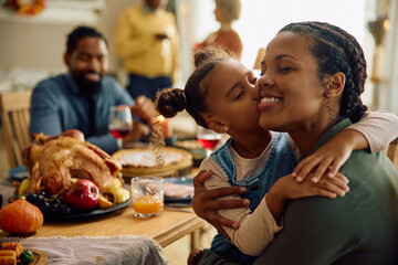 Grateful black girl kisses her mother during Thanksgiving family meal. - Powered by Adobe