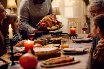 Close up of father serving roast turkey while having Thanksgiving meal with his family.