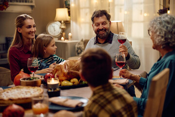 Happy father raising a toast during Thanksgiving dinner with his family at dining table.