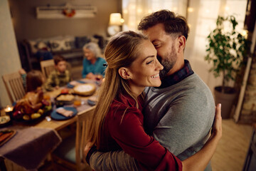 Happy couple embraces while celebrating Thanksgiving with their family at home.