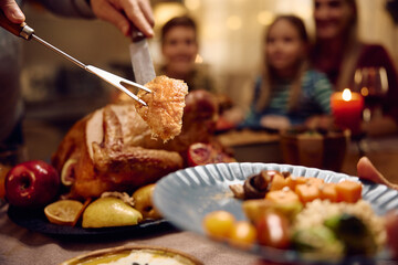 Close up of father carving Thanksgiving turkey during family dinner at dining table. - obrazy, fototapety, plakaty