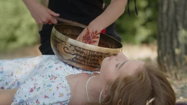 A shaman girl performs a cleansing ritual for prosperity, longevity and fulfillment of desires. Oriental healer uses tibetan singing brass bowl and handmade wand. Woman patient, undergoing music