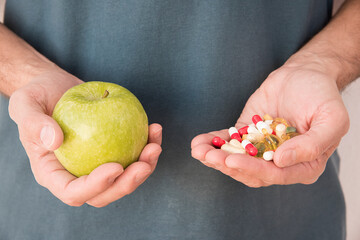 man's hand with one with a green apple and hand with pills 