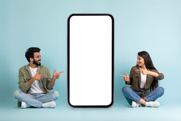 Excited eastern couple pointing at giant smartphone with mockup