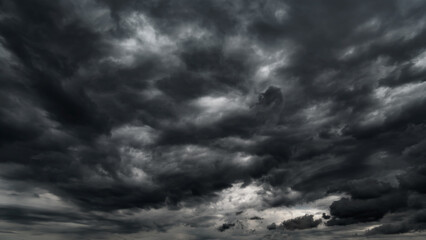 dark dramatic sky with black stormy clouds before rain or snow as abstract background, extreme weather, the sun shines through the clouds, high contrast photo