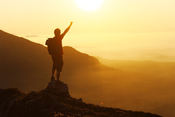 Silhouette of a mountaineer man with his fist raised in victory celebrating his ascension to a...