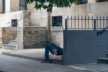Homeless person lying on an old matrass, legs only visible, in the recess of a brick building with...
