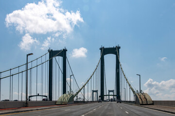 Fototapeta na wymiar Drivers perspective on Delaware Memorial Bridge near Wilmington, DE, USA in northerly direction with cars on road crossing the Delaware River against a blue sky