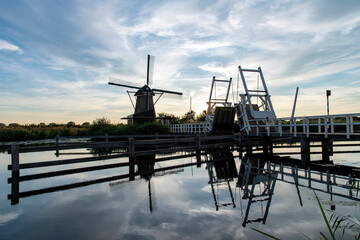 Fototapeta premium Sunset view over tranquil water in canal with perfect reflection of drawing bridge and one of the iconic 18th-century windmills in Kinderdijk, the Netherlands; UNESCO World Heritage site