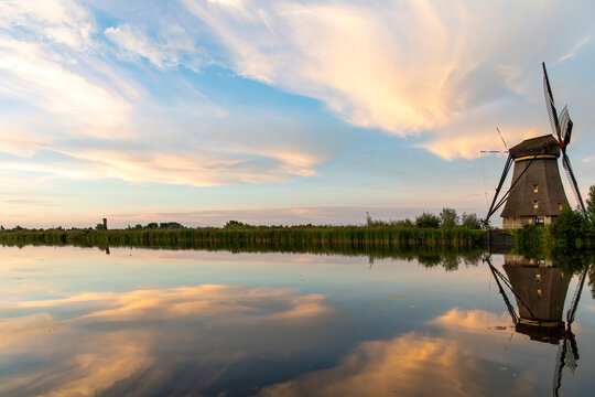 Typical Dutch windmill along long row of reed beds in the Kinderdijk area, the Netherlands with a near perfect reflection of the windmill, reed beds and clouds in the tranquil water during sunset
