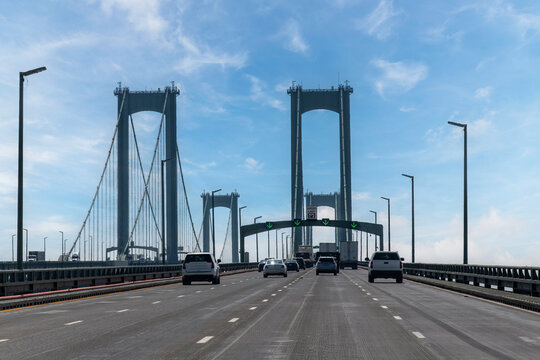 Drivers perspective on Delaware Memorial Bridge near Wilmington, DE, USA in northerly direction with cars on road crossing the Delaware River against a blue sky