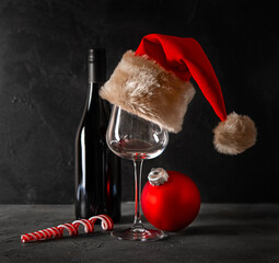 Christmas card. Wine bottle, glass, Santa hat, lollipop on a dark background