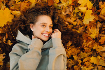 Smiling young woman lying on the autumn foliage in the forest with the yellow leaves