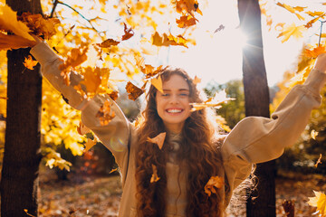 Smiling young woman throw up the autumn leaves in the forest at sunset