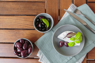 Feta cheese sliced on gray plate with black olives and basil leaves. Delicious and healthy breakfast on terrace