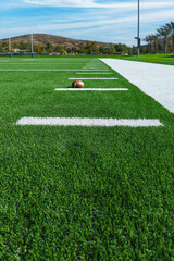View looking down the sideline of an American football field with line markers and football.