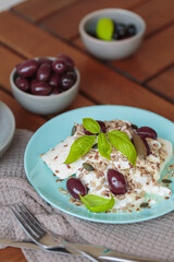 Feta cheese sliced on blue plate with sesame, flax seeds, served with black olives and basil leaves. Delicious and healthy breakfast on terrace