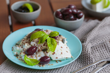 Feta cheese sliced on blue plate with sesame, flax seeds, served with black olives and basil leaves. Delicious and healthy breakfast on terrace