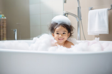 bath time, little asian child girl taking bubble bath in beautiful bathroom, Kids hygiene, Shampoo, hair treatment and soap for children, Kid bathing in large tub , foam in hair - obrazy, fototapety, plakaty