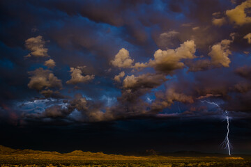 Dreamy lightning strike in the desert, bathing the stormy sky with rich hues and shades of electric blue.