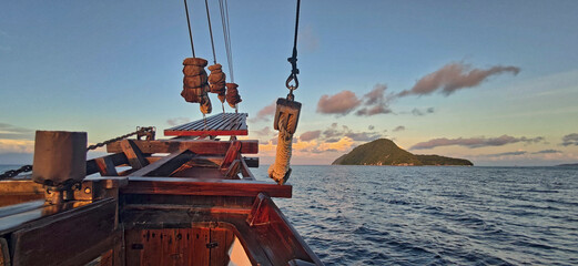 Panoramic image of the bow of a sailing boat leading to an isolated and green island in a tropical...