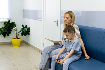 Happy toddler boy with a woman mother in the clinic waiting for a doctor s appointment. Mom with a...