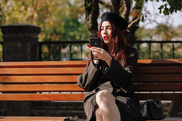 Girl sits on a bench and paints her lips in an autumn park