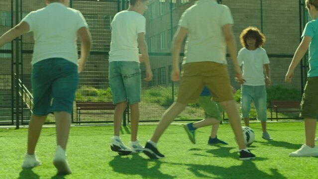 Group of boys playing football on  sport playground in sunny day . Many kids play soccer in stadium with green grass and gate . Training , competition , healthy activity for children . Slow motion