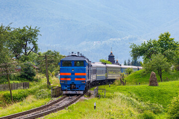 Powerful diesel locomotive pulls passenger train. Railway in the mountains.