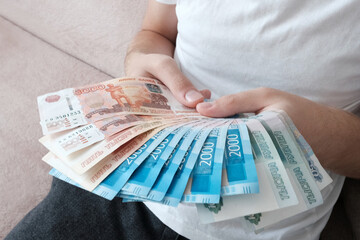 A European young man holds Russian paper banknotes in his hands, rubles in denominations of 1000,...