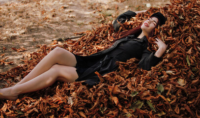 A woman in retro coat lying in autumn leaves