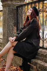 A girl in retro coat posing sitting on fence in the autumn park