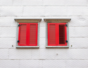 Fototapeta premium two red wooden shutters on a white facade in the style of wooden shingle siding